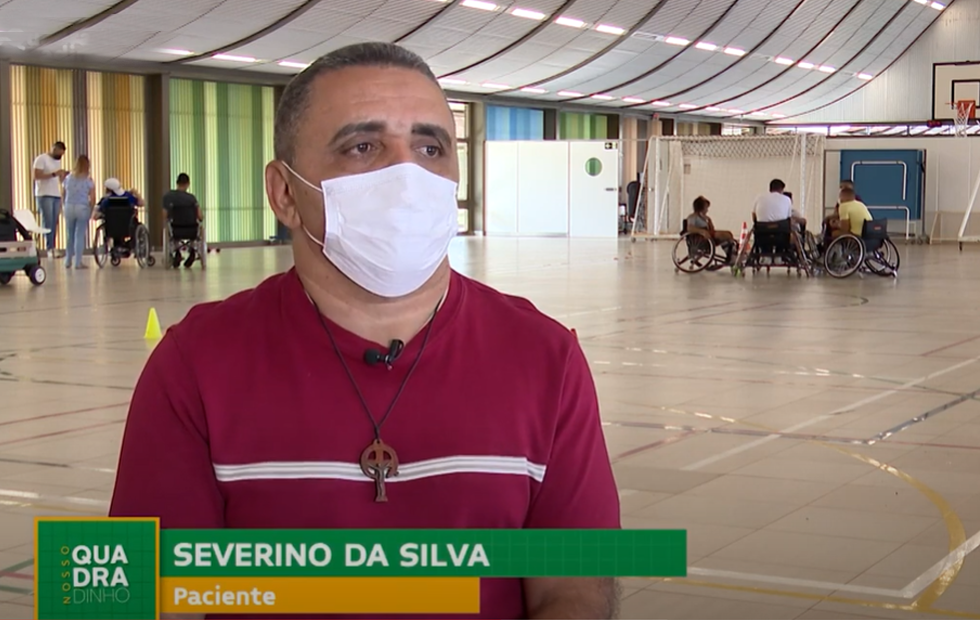 De camisa vermelha, o paciente e jogador de rugy em cadeira de rodas Severino da Silva fala sobre sua reabilitação. Ao fundo, na quadra poliesportiva do Hospital SARAH Lago Norte, outros cadeirantes conversam em grupos.