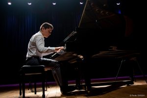 Trajando camisa e calça sociais cinza e sentado ao piano de cauda, o pianista Aleyson Scopel apresenta-se no Teatro SARAH.