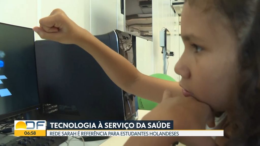 Captura de tela do Bom Dia DF, da TV Globo, mostra garoto exercitando o braço direito com jogo de computador no laboratório de realidade virtual do SARAH Brasília Lago Norte.