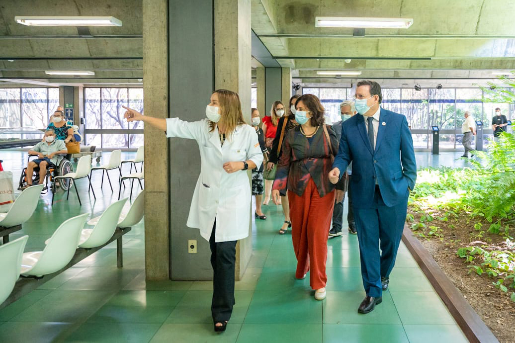 Vestindo jaleco branco, Dra. Lúcia Willadino Braga apresenta o ambulatório do SARAH Brasília Centro à ministra da Saúde, Nísia Trindade, vestindo blusa de manga comprida em tons de vermelho e azul com calças vermelhas, e ao secretário-executivo da Saúde, Swedenberger Barbosa, vestindo terno azul e gravata. Ao fundo, membros da comitiva ministerial e da equipe do hospital acompanham a visita.