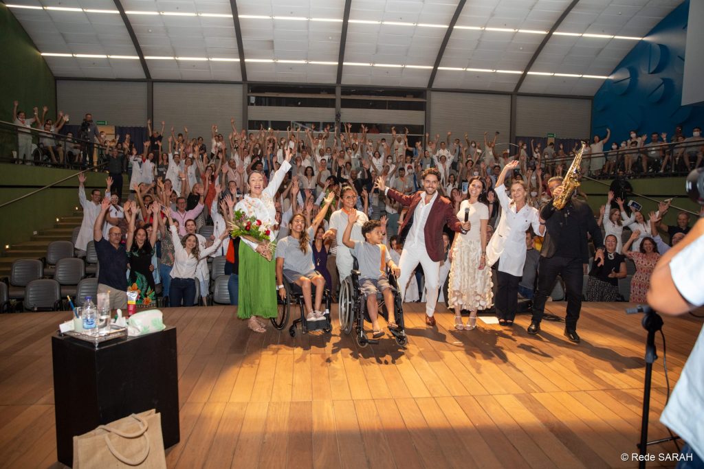 Thiago Arancam e Angélica Cruz posando para foto junto à Dra. Lúcia Willadino Braga e o público do Teatro SARAH Thiago Arancam e Angélica Cruz posando para foto junto à Dra. Lúcia Willadino Braga e o público do Teatro SARAH